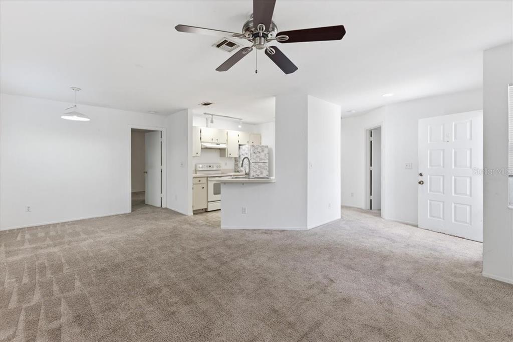 An open-concept living room with beige carpeting, a ceiling fan, and an adjacent kitchen — 9410 TACOMA AVENUE UNIT A, ENGLEWOOD, FL