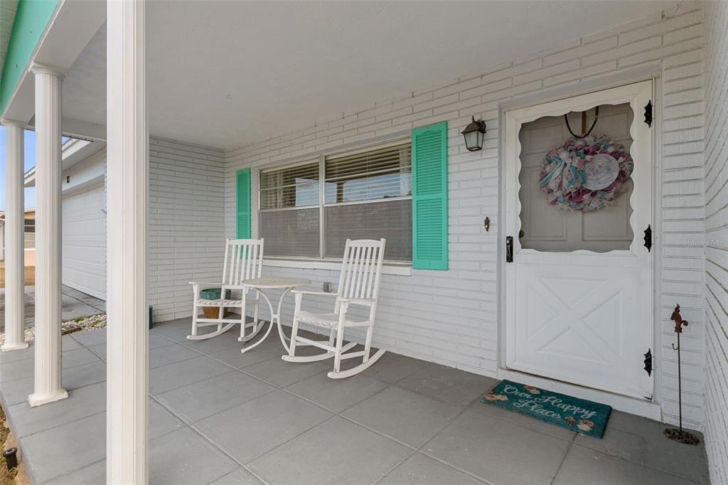 A covered front porch features white brick walls, teal shutters, and two white rocking chairs — 83 S HARRISON STREET, BEVERLY HILLS, FL