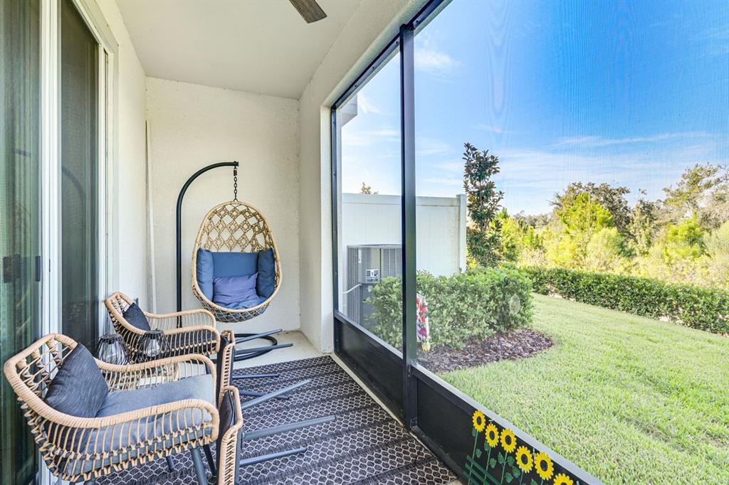 A screened-in patio features wicker chairs, a hanging egg chair, and a view of grass — 5443 ELMVIEW CROSSING, WESLEY CHAPEL, FL