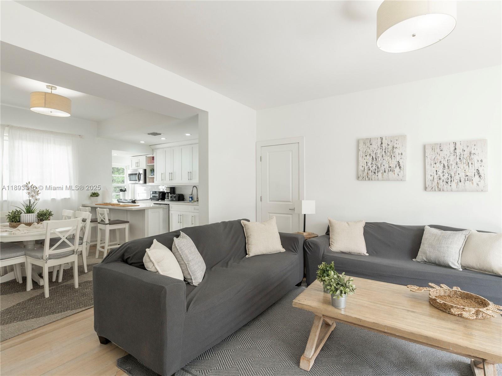 A living room with gray sofas and a dining area opens into a white kitchen — 241 28th St # 1, Miami Beach FL 33140, MIAMI BEACH, FL