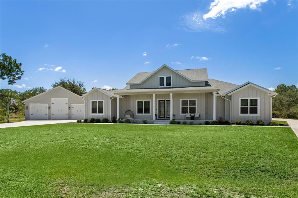 A light gray farmhouse-style house with a detached garage and a large front lawn — 8408 WOODLEAF BOULEVARD, WESLEY CHAPEL, FL