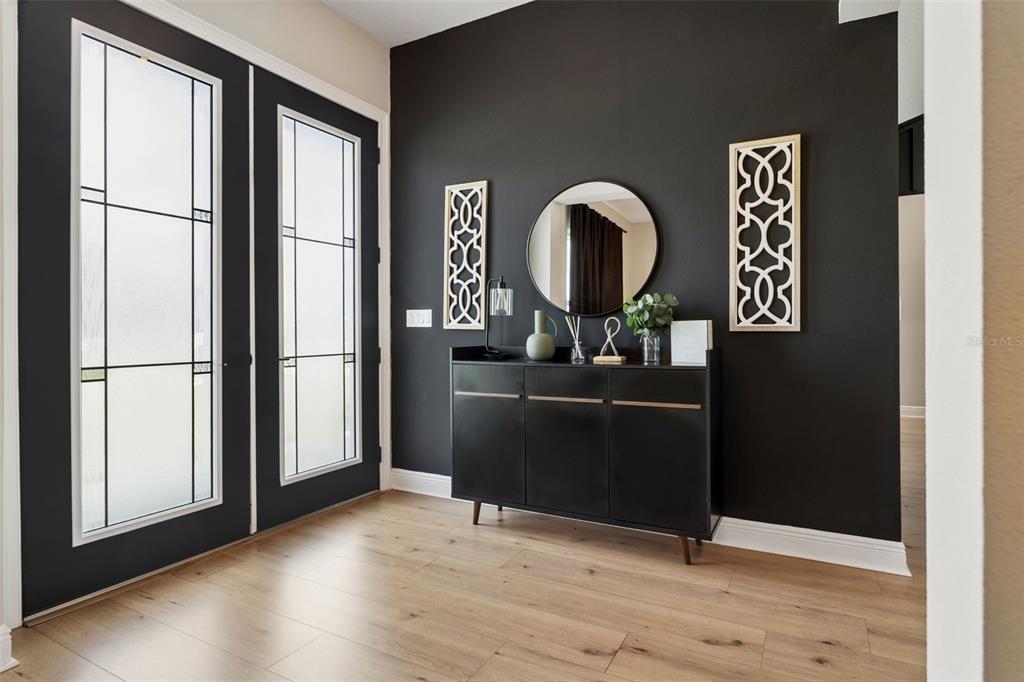 A modern entryway features a black accent wall, a dark sideboard, and double glass doors — 8408 WOODLEAF BOULEVARD, WESLEY CHAPEL, FL