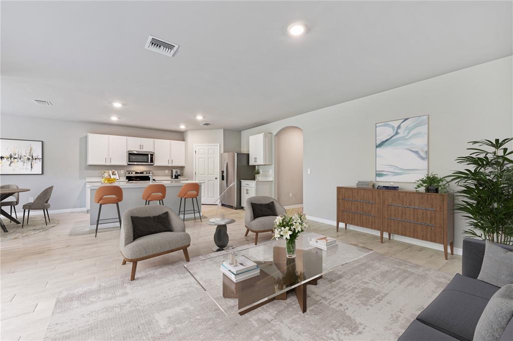 An open-concept living room and kitchen featuring light wood flooring, white cabinetry, and modern furniture — 25110 ALCAZAR DRIVE, PUNTA GORDA, FL