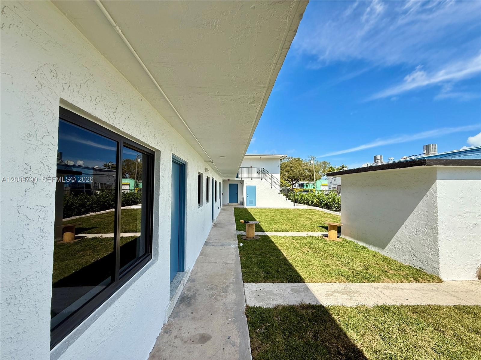 An exterior view shows a white building with blue doors, a concrete walkway, and a grassy courtyard — 180 NE 57th St # 4, Miami FL 33137, MIAMI, FL