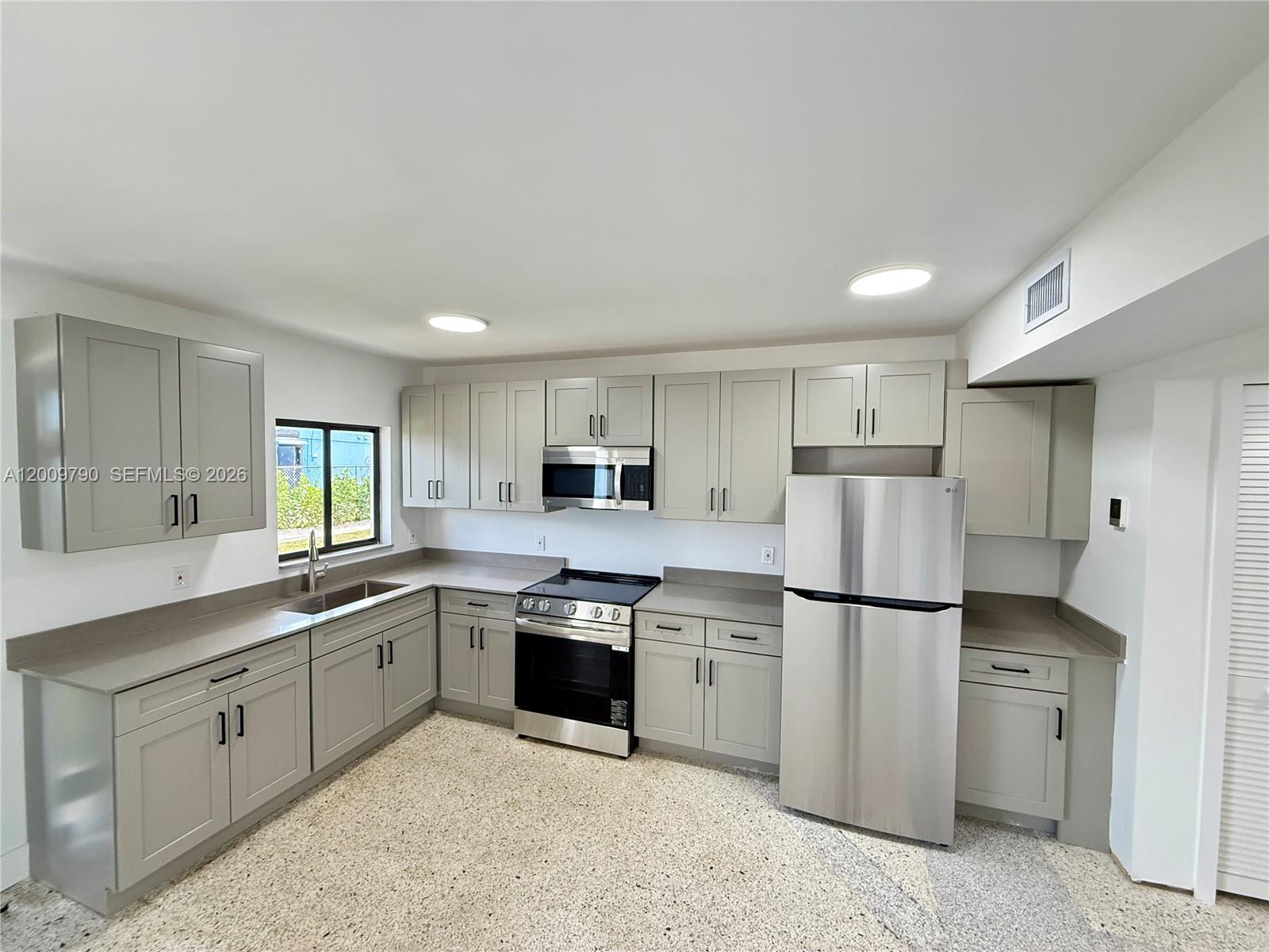 A kitchen features gray cabinets, stainless steel appliances, and speckled flooring — 180 NE 57th St # 4, Miami FL 33137, MIAMI, FL