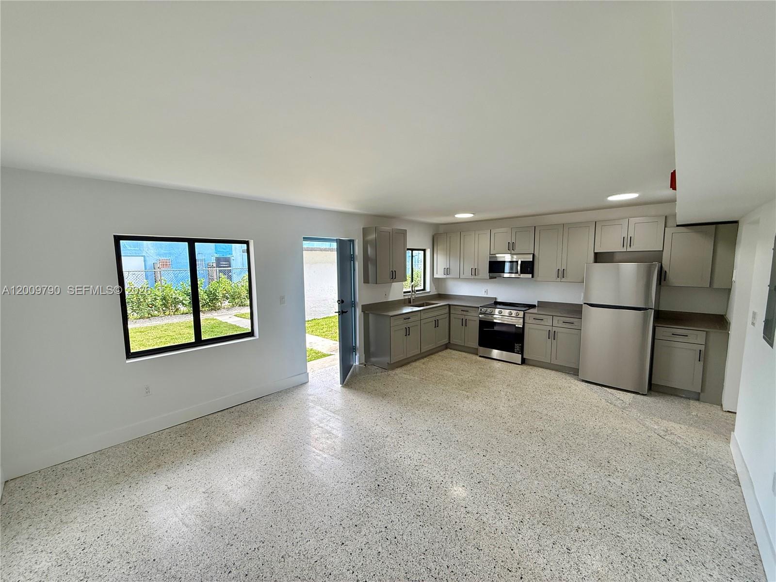 An open-concept kitchen features gray cabinetry, stainless steel appliances, and terrazzo flooring — 180 NE 57th St # 4, Miami FL 33137, MIAMI, FL