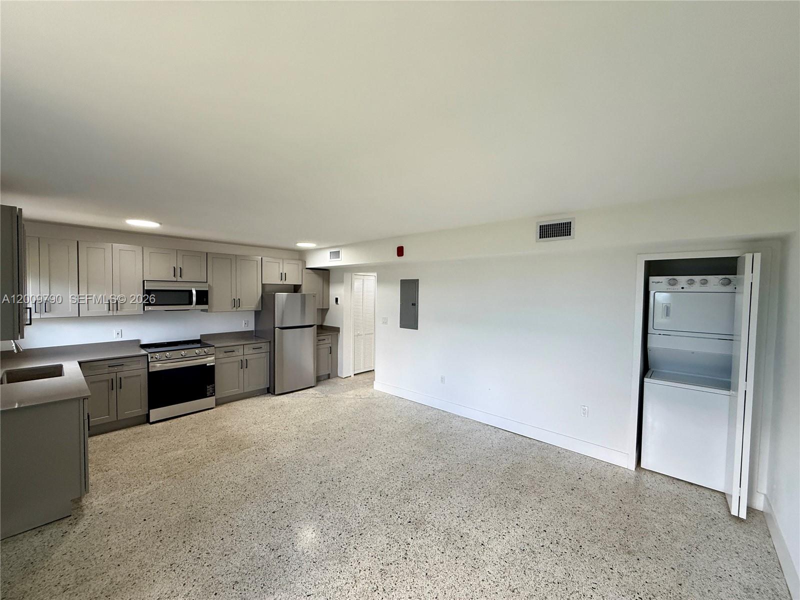 A kitchen with grey cabinets, stainless steel appliances, and a stacked washer-dryer unit — 180 NE 57th St # 4, Miami FL 33137, MIAMI, FL
