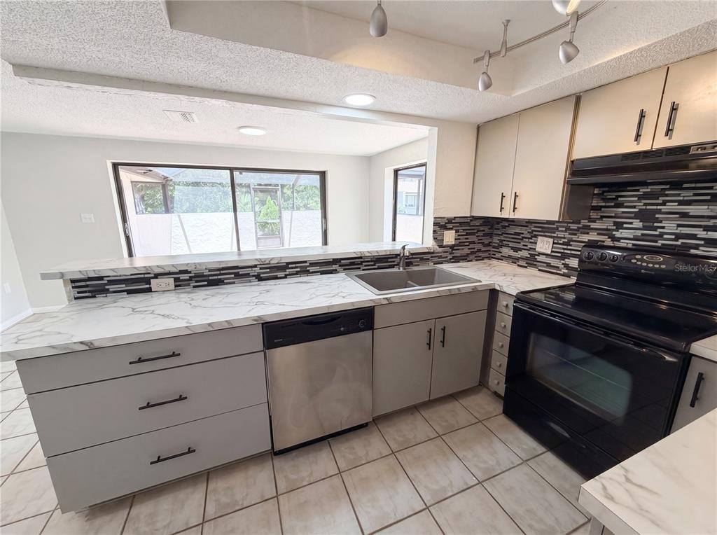A kitchen features gray cabinets, marble-look countertops, stainless steel appliances, and a tiled backsplash — 8 BUMELIA COURT, HOMOSASSA, FL