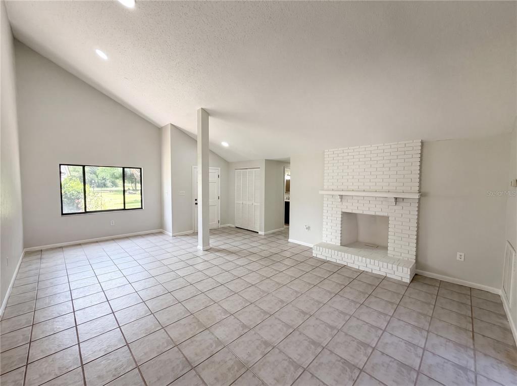 A living room with vaulted ceilings, tile flooring, and a white painted brick fireplace — 8 BUMELIA COURT, HOMOSASSA, FL