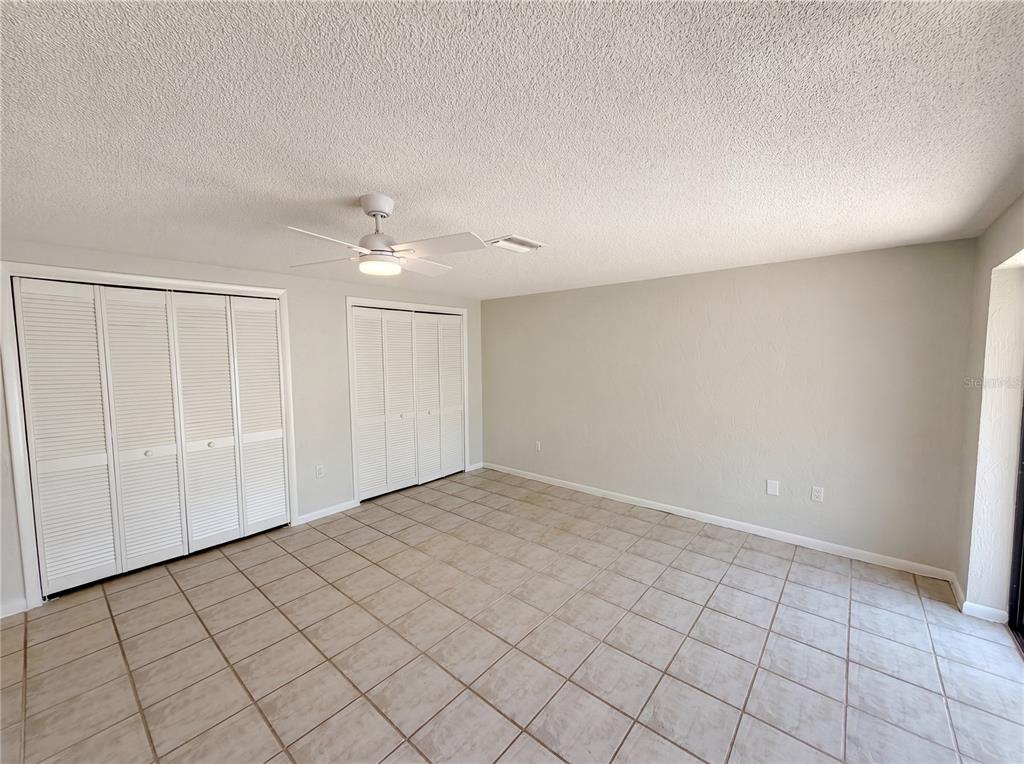A room with light-colored walls, tiled flooring, two sets of white louvered closet doors, and a ceiling fan — 8 BUMELIA COURT, HOMOSASSA, FL