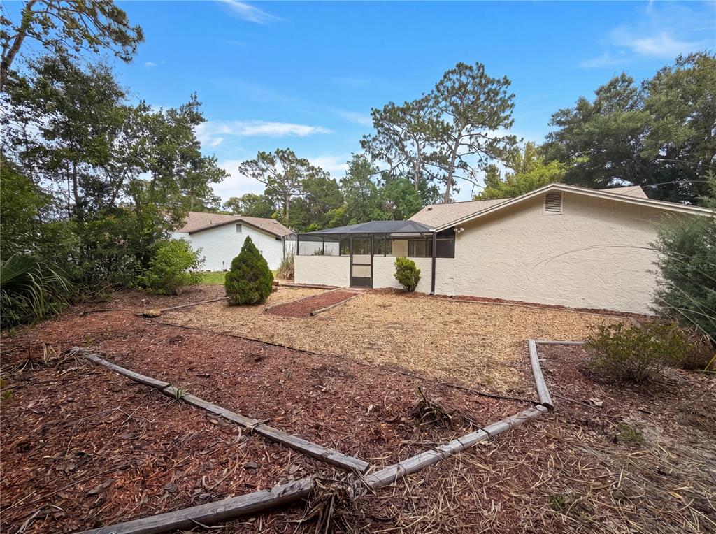 A backyard features a screened-in patio, wood-chip landscaping, and a wooden border frame — 8 BUMELIA COURT, HOMOSASSA, FL