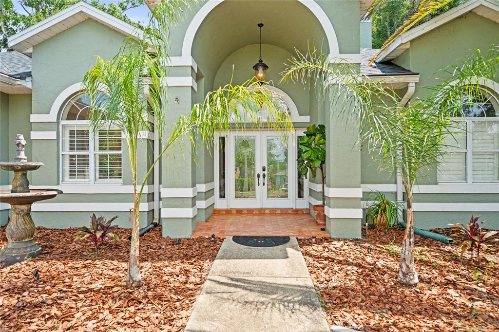 The exterior of a green house features a paved walkway leading to a double-door entrance — 1254 MAGNOLIA FARMS CT, EUSTIS, FL