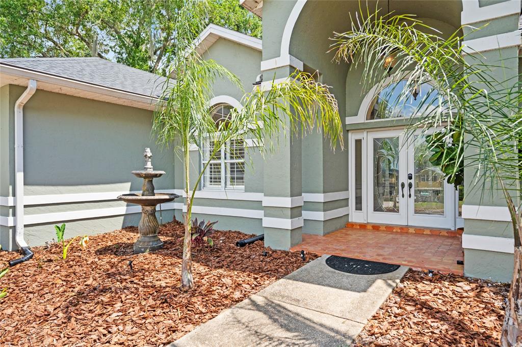 The exterior of a house features a stone fountain, a palm tree, and a double-door entrance — 1254 MAGNOLIA FARMS CT, EUSTIS, FL