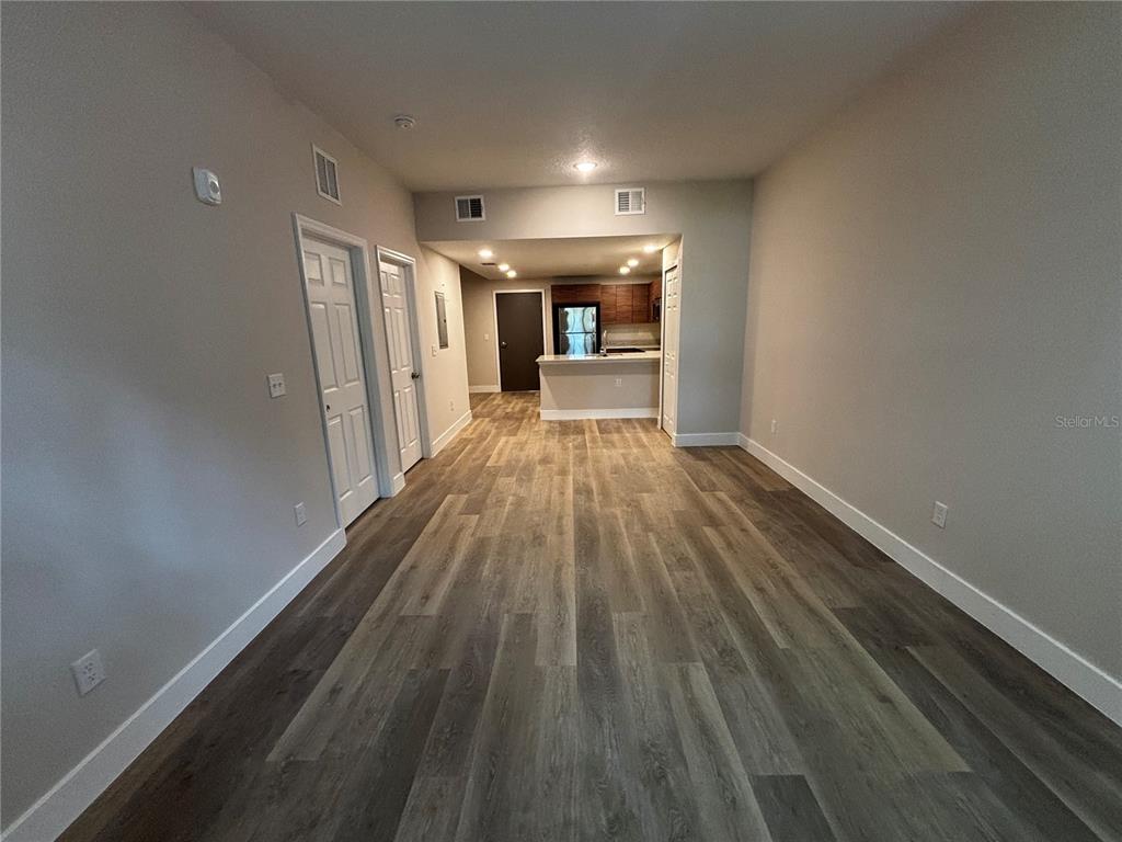 An interior view of an open-concept living area with wood-look flooring and a kitchen beyond — 4424 S TEXAS AVENUE UNIT 111, ORLANDO, FL