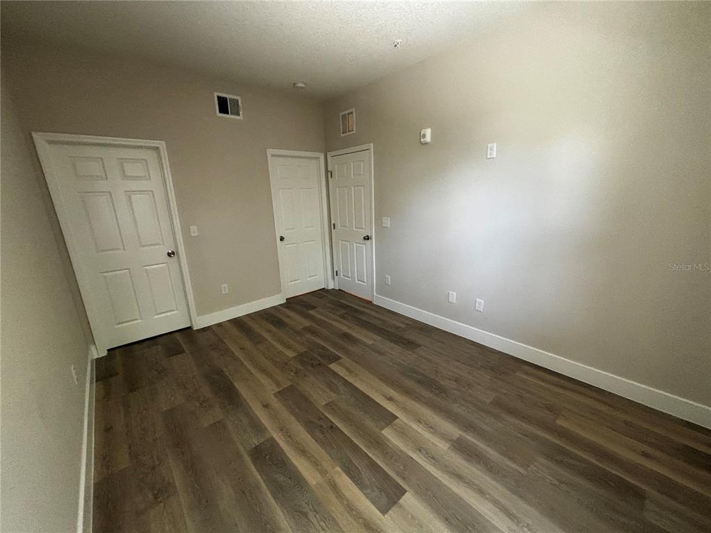 An empty room features light-colored walls, wood-look flooring, and three white interior doors — 4424 S TEXAS AVENUE UNIT 111, ORLANDO, FL