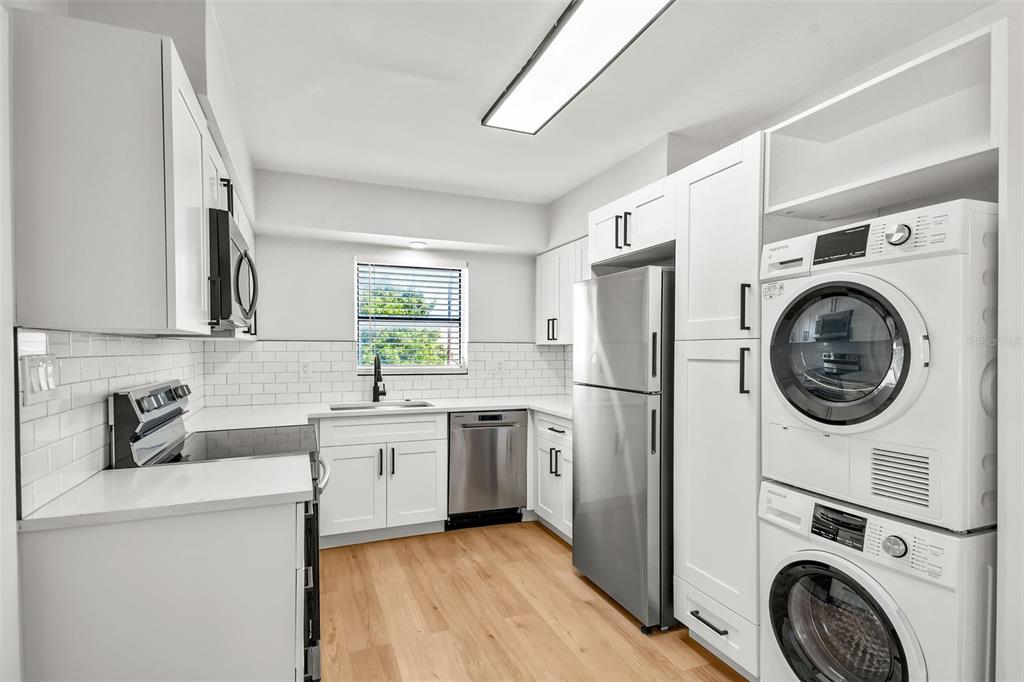 A modern kitchen features white cabinets, stainless steel appliances, a subway tile backsplash, and laundry units — 300 S NIMBUS AVENUE UNIT 6, CLEARWATER, FL