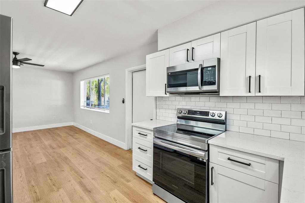A kitchen with white cabinets, stainless steel appliances, and subway tile backsplash opens to a room — 300 S NIMBUS AVENUE UNIT 6, CLEARWATER, FL