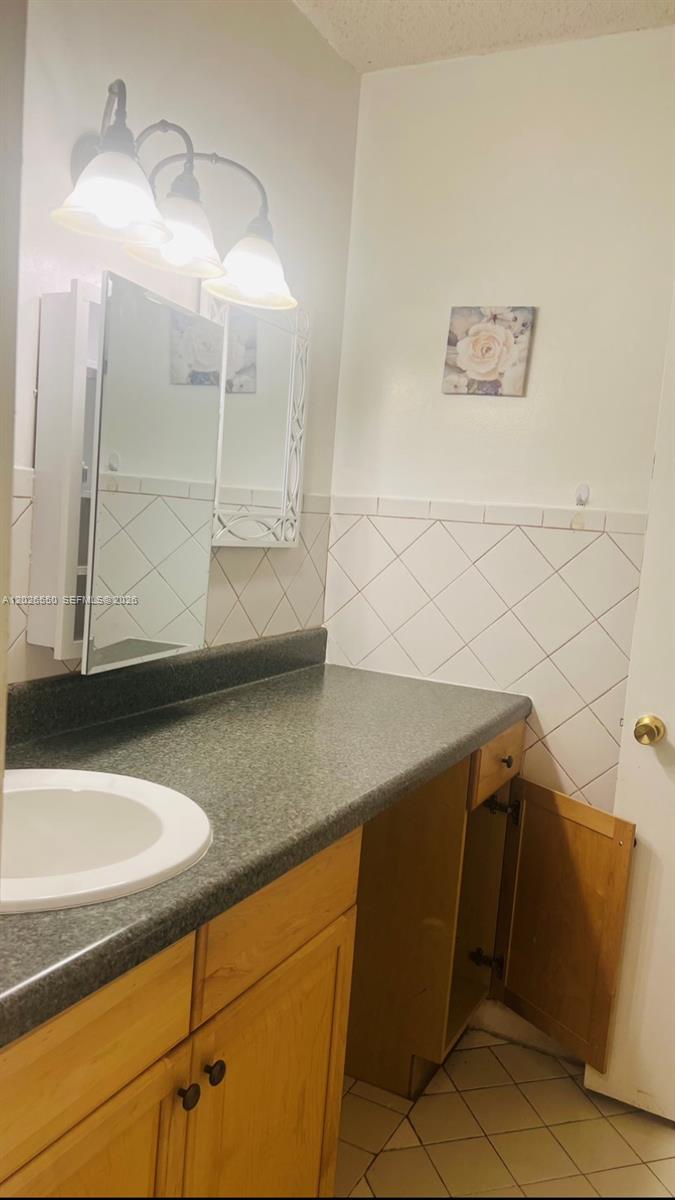 A bathroom vanity features a dark countertop, light wood cabinets, and a wall-mounted mirror — 6505 Winfield Blvd # 53, Margate FL 33063, MARGATE, FL