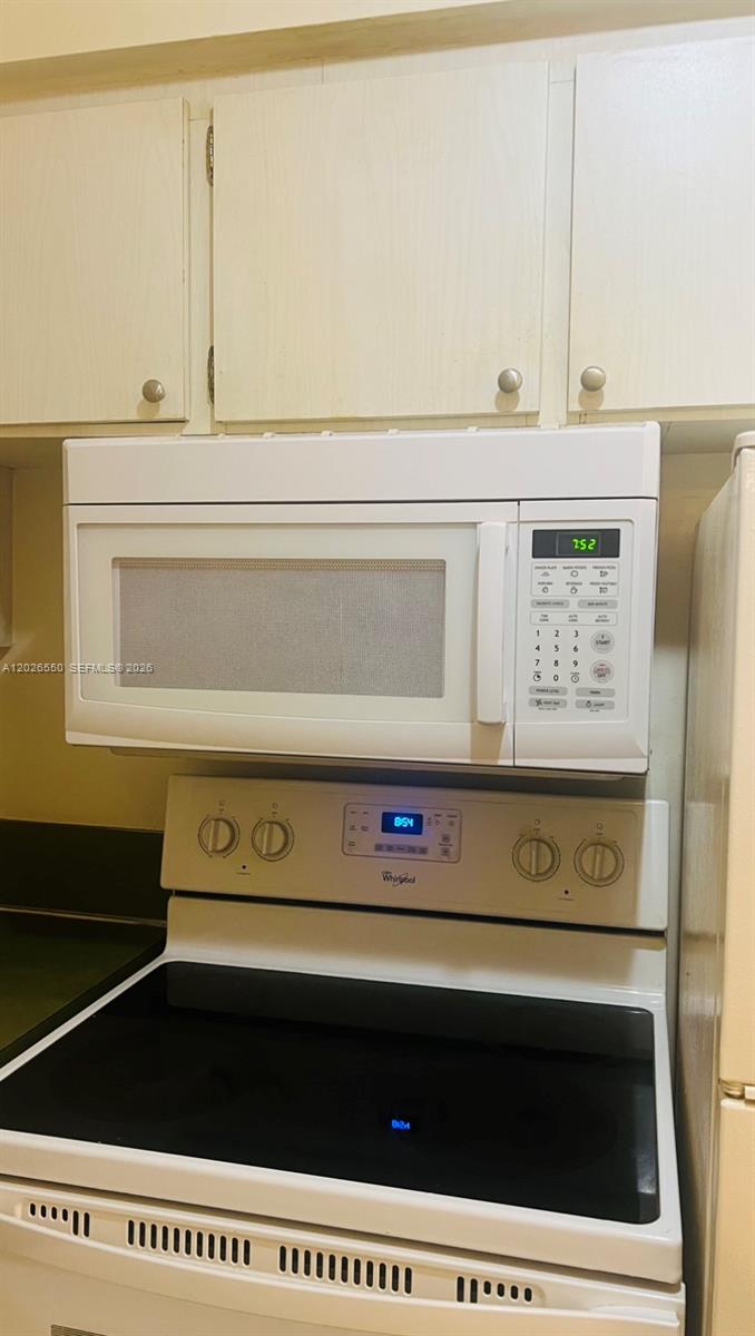A white over-the-range microwave is mounted above a white electric stove in a kitchen — 6505 Winfield Blvd # 53, Margate FL 33063, MARGATE, FL