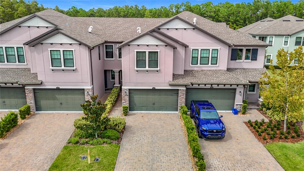 An aerial view shows three attached townhomes with paved driveways and a blue pickup truck — 4868 SAN MARTINO DRIVE, WESLEY CHAPEL, FL