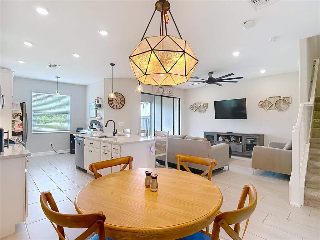 An open-concept kitchen and living area features a round wooden dining table and pendant lighting — 4868 SAN MARTINO DRIVE, WESLEY CHAPEL, FL