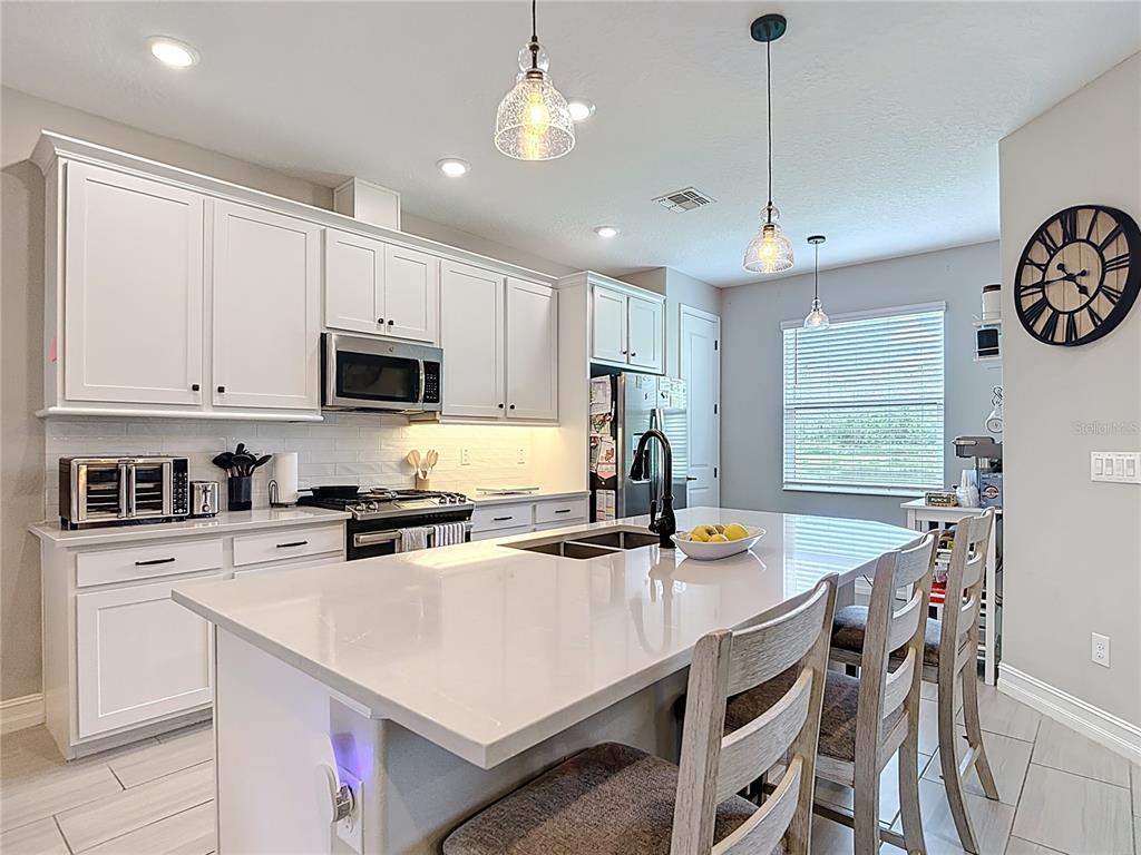 A modern kitchen features white cabinetry, a large quartz-topped island, and stainless steel appliances — 4868 SAN MARTINO DRIVE, WESLEY CHAPEL, FL