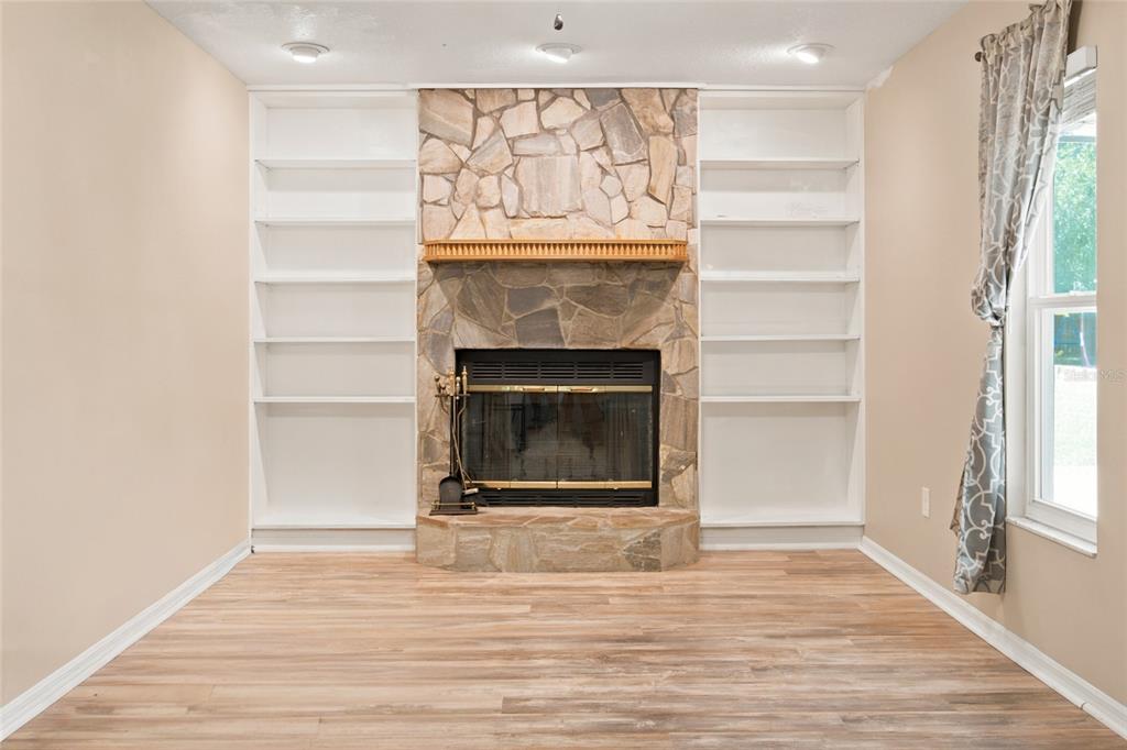 A living room features a stone fireplace flanked by white built-in bookshelves and wood flooring — 500 NE 52ND COURT, OCALA, FL