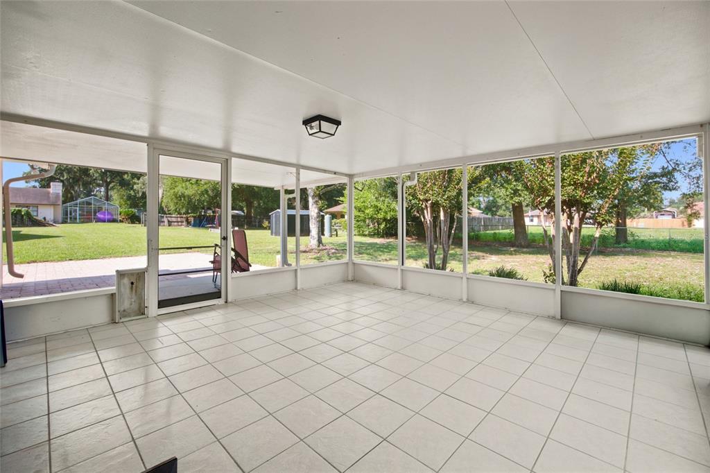 A tiled, screened-in porch overlooks a large backyard with trees and a neighboring house — 500 NE 52ND COURT, OCALA, FL