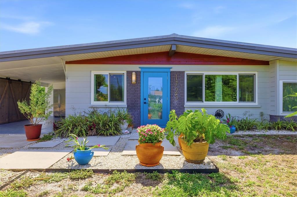 The exterior of a mid-century modern home features a bright blue door and gravel landscaping — 1725 MEL O DE LANE, ENGLEWOOD, FL