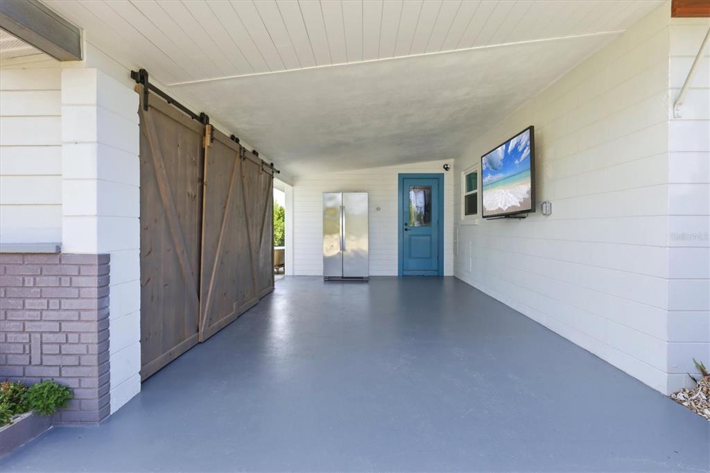 A covered patio features a gray floor, a blue door, a refrigerator, and a wall-mounted television — 1725 MEL O DE LANE, ENGLEWOOD, FL