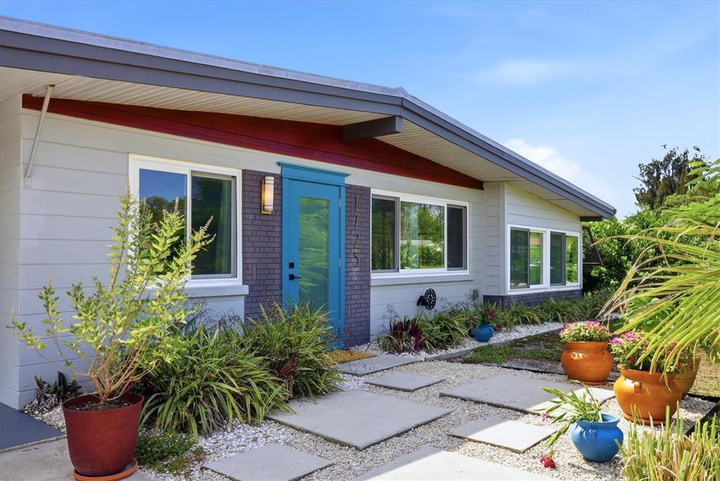 A single-story house with gray siding, a blue front door, and a gravel front yard — 1725 MEL O DE LANE, ENGLEWOOD, FL
