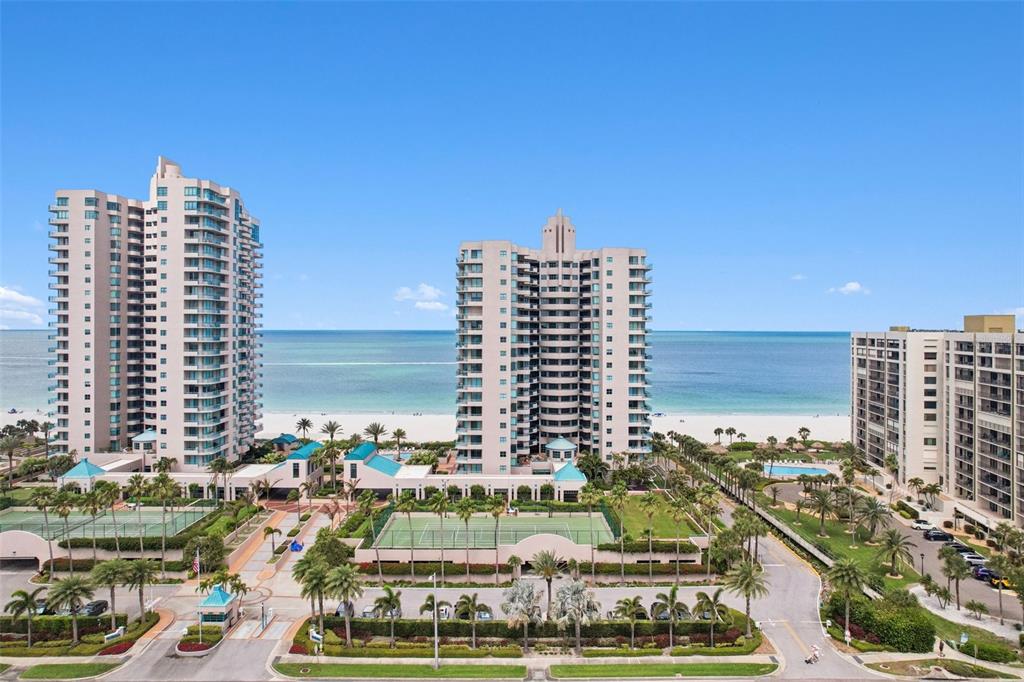 An aerial view shows three high-rise residential buildings situated along a sandy beach — 1520 GULF BOULEVARD UNIT 202, CLEARWATER BEACH, FL