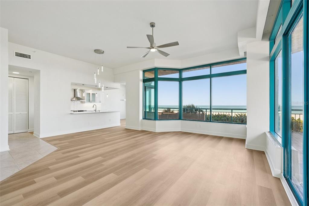 An open-concept living area features light wood flooring, a ceiling fan, and floor-to-ceiling ocean views — 1520 GULF BOULEVARD UNIT 202, CLEARWATER BEACH, FL
