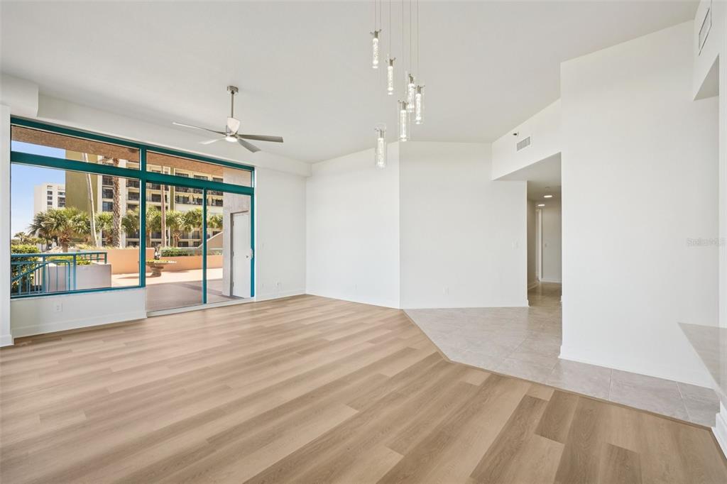 An empty living room features light wood flooring, a ceiling fan, and a glass balcony door — 1520 GULF BOULEVARD UNIT 202, CLEARWATER BEACH, FL