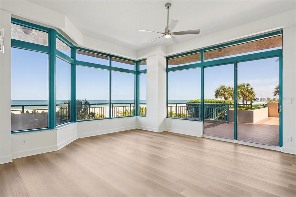 An empty room features light wood floors, a ceiling fan, and large windows overlooking the ocean — 1520 GULF BOULEVARD UNIT 202, CLEARWATER BEACH, FL