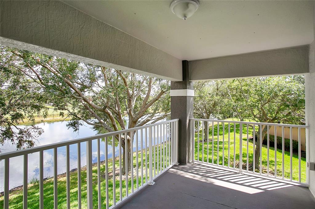 A covered balcony with a white metal railing overlooks a grassy area and a pond — 13815 FAIRWAY ISLAND DRIVE UNIT 1328, ORLANDO, FL