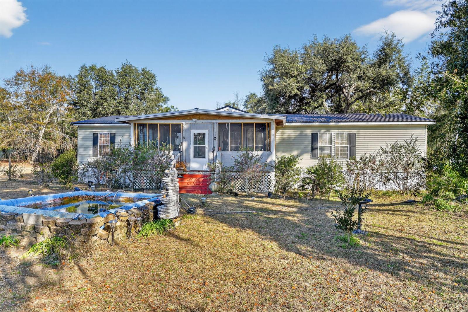 A single-story manufactured home with a screened front porch and a stone-bordered pond in front — 7638 Sundown Creek Road, FL 32331, FL