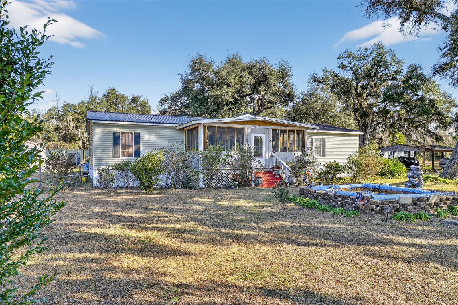 A single-story manufactured home with a screened-in porch and a stone-bordered pond in front — 7638 Sundown Creek Road, FL 32331, FL