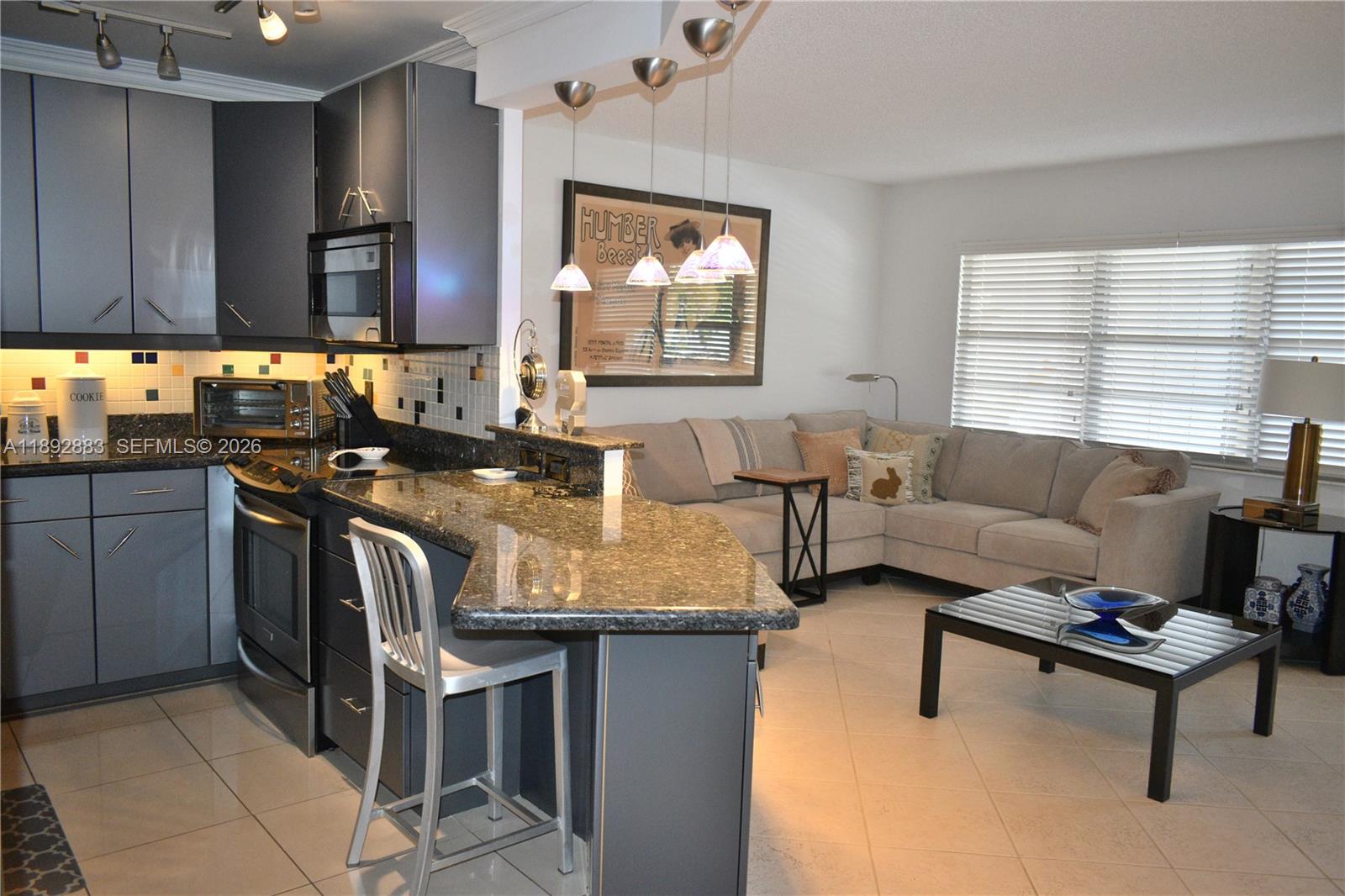 A kitchen with dark cabinets and granite countertops opens into a living room with seating — 2011 Cornwall # A, Boca Raton FL 33434, BOCA RATON, FL