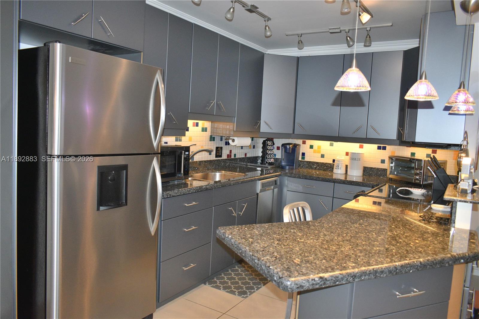 A kitchen features gray cabinets, granite countertops, stainless steel appliances, and a colorful tiled backsplash — 2011 Cornwall # A, Boca Raton FL 33434, BOCA RATON, FL