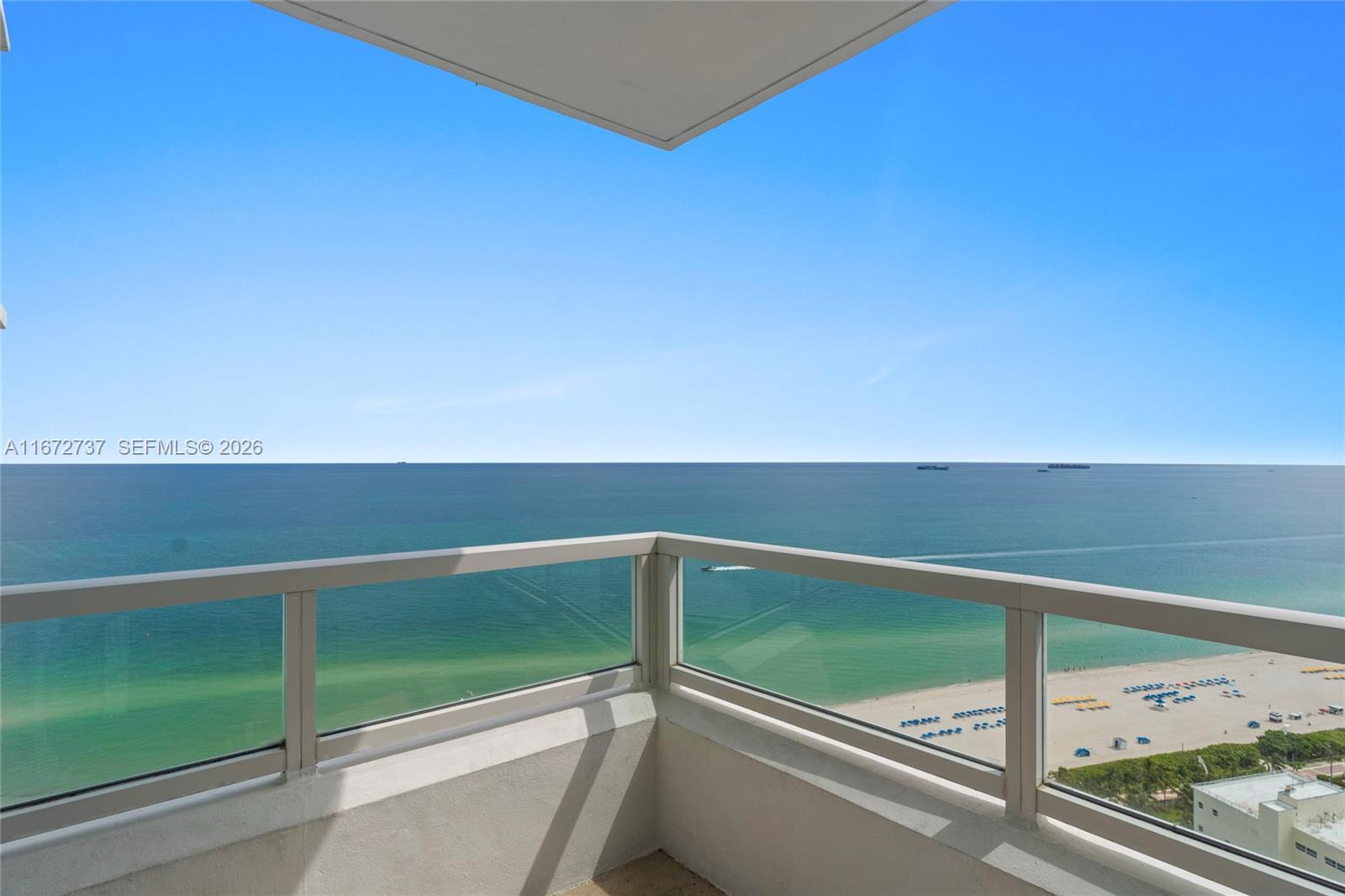 A high-rise balcony overlooks a sandy beach and the ocean under a clear blue sky — 4401 Collins Ave, Miami Beach FL 33140, MIAMI BEACH, FL