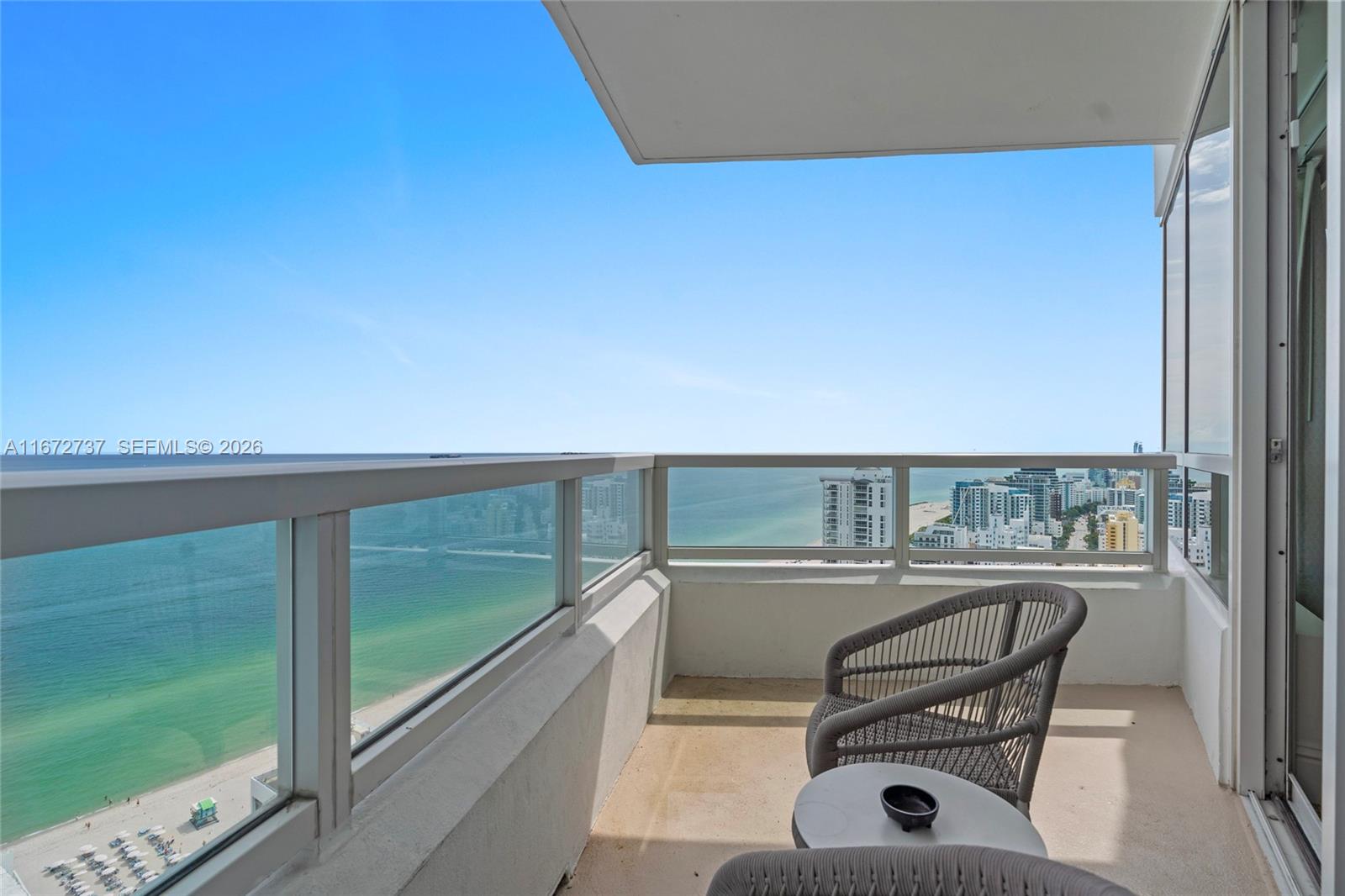A balcony with glass railings overlooks the ocean and a beach with city buildings — 4401 Collins Ave, Miami Beach FL 33140, MIAMI BEACH, FL