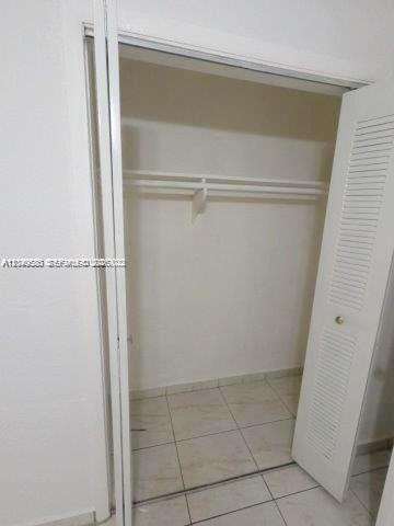 A white closet with a shelf and hanging rod features tiled flooring and louvered doors — 3062 NW 60th St, Miami FL 33142, MIAMI, FL