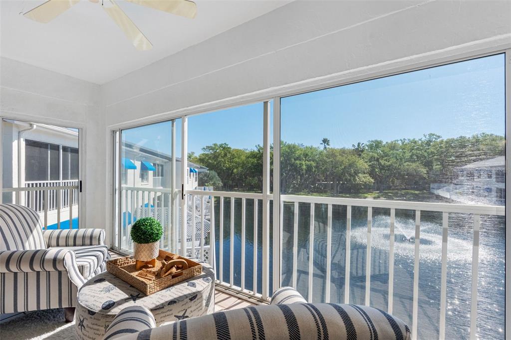 A sunroom with striped armchairs overlooks a pond with a fountain through large sliding windows — 11351 SHIPWATCH LANE UNIT 1841, LARGO, FL