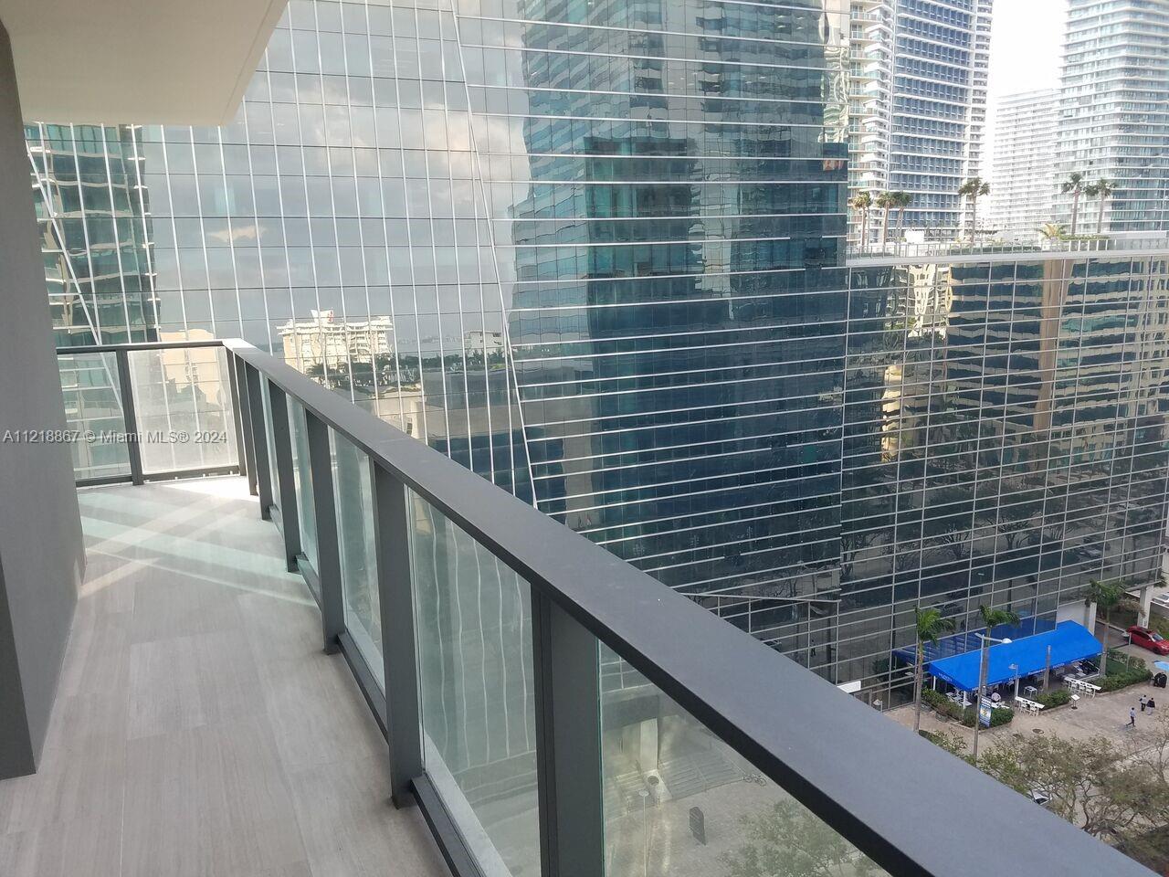 A balcony with a glass railing overlooks a city street and surrounding glass skyscrapers — 1451 Brickell Ave # 1206, Miami FL 33131, MIAMI, FL