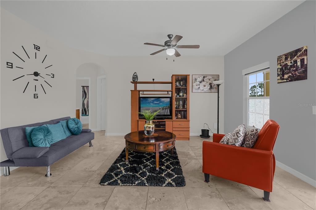 A living room features tile flooring, a large wall clock, and an orange armchair — 2309 BETSY ROSS LANE UNIT 2309, ST CLOUD, FL