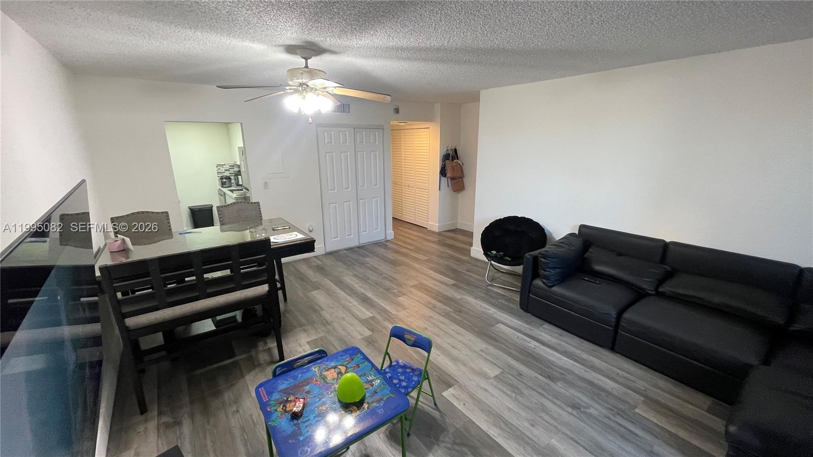 An empty living room features gray wood-look flooring, a ceiling fan, and sliding glass doors — 10801 SW 109th Ct # D108, Miami FL 33176, MIAMI, FL