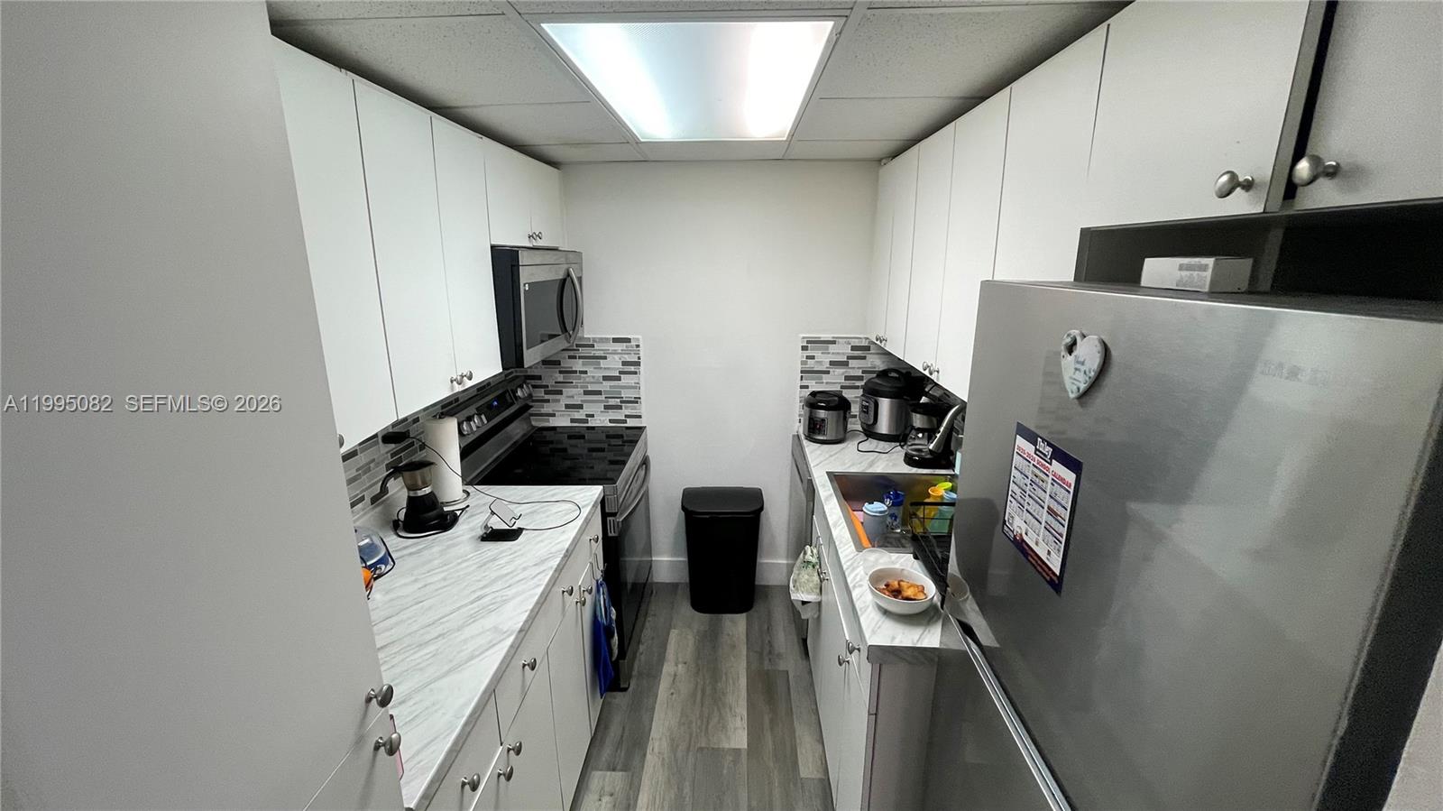 A galley kitchen features white cabinets, marble-look countertops, stainless steel appliances, and gray flooring — 10801 SW 109th Ct # D108, Miami FL 33176, MIAMI, FL