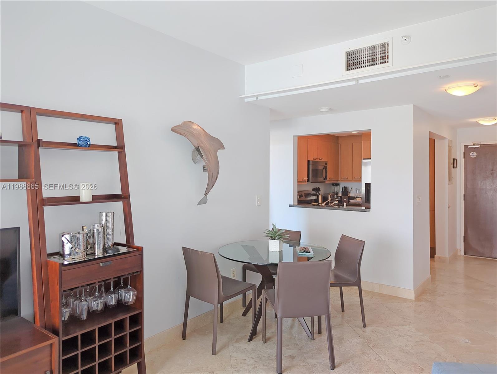 A dining area with a glass table, four chairs, and a wooden shelving unit — 225 Collins Ave # 4J, Miami Beach FL 33139, MIAMI BEACH, FL