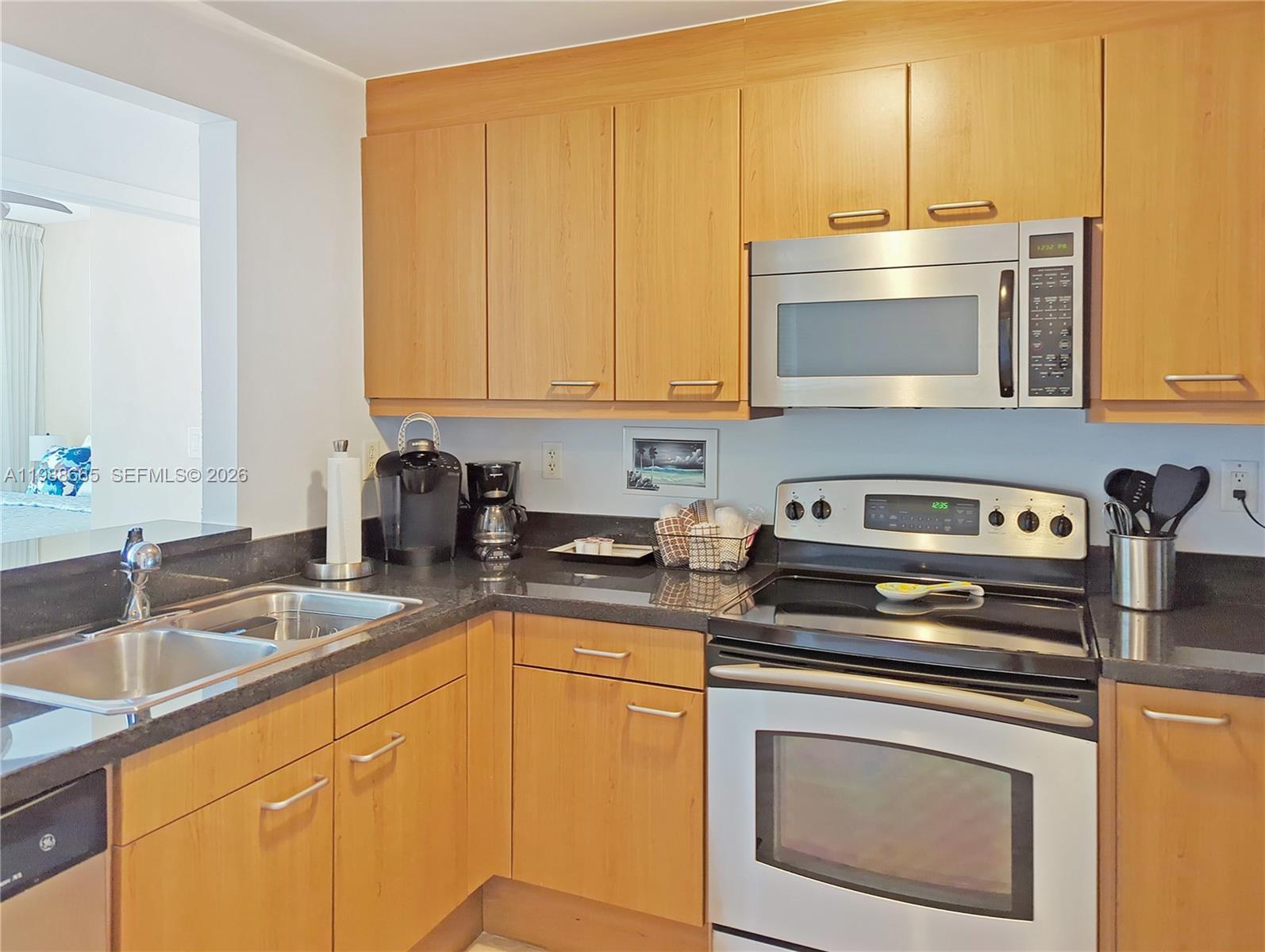 A kitchen features light wood cabinets, black countertops, and stainless steel appliances — 225 Collins Ave # 4J, Miami Beach FL 33139, MIAMI BEACH, FL